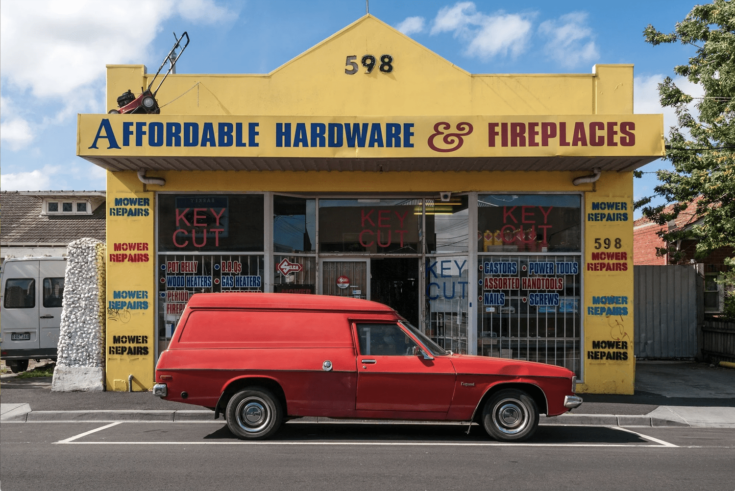 A red vintage panel van outside the yellow Affordable Hardware and Fireplaces shopfront in West Footscray